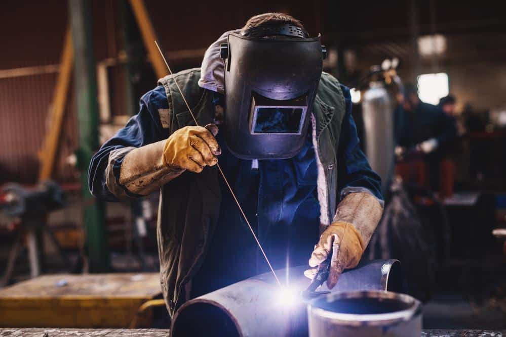 Welder in protective uniform and mask welding metal pipe on the